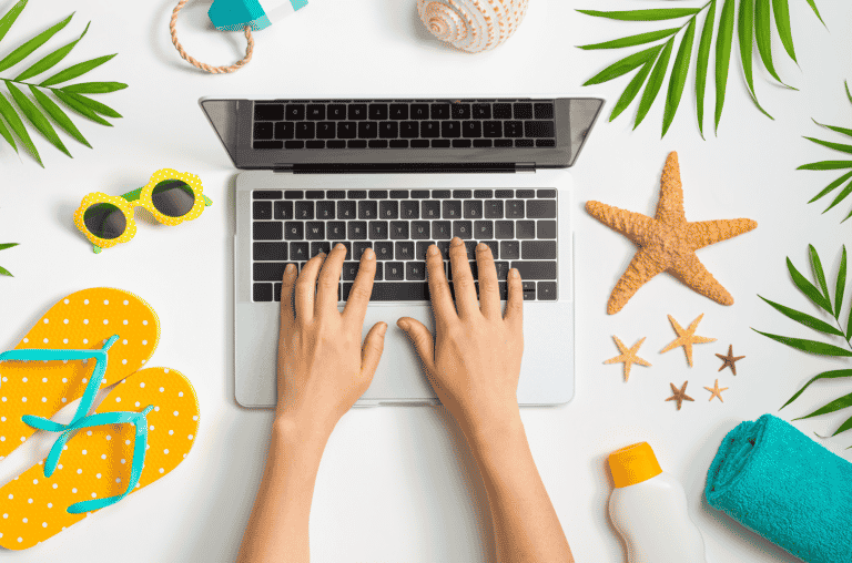 Hände am Laptop, außenrum Urlaubsgegenstände, symbolisiert Urlaubszeit