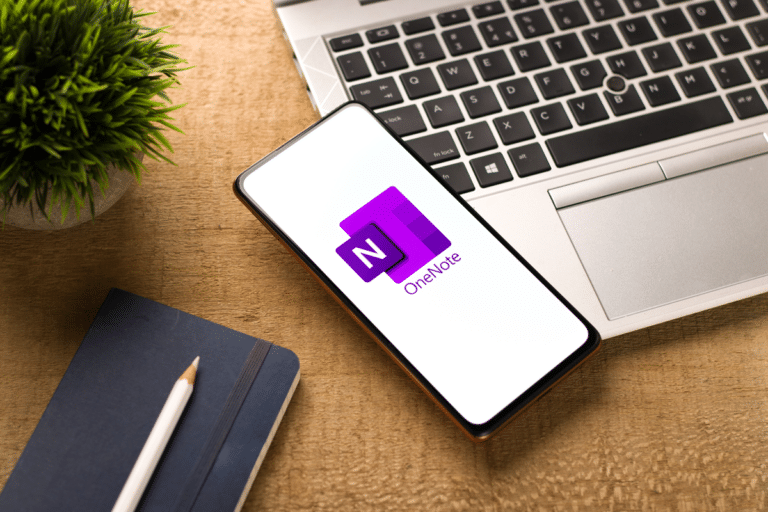Laptop und Handy auf dem Schreibtisch, OneNote Logo auf dem Bildschirm