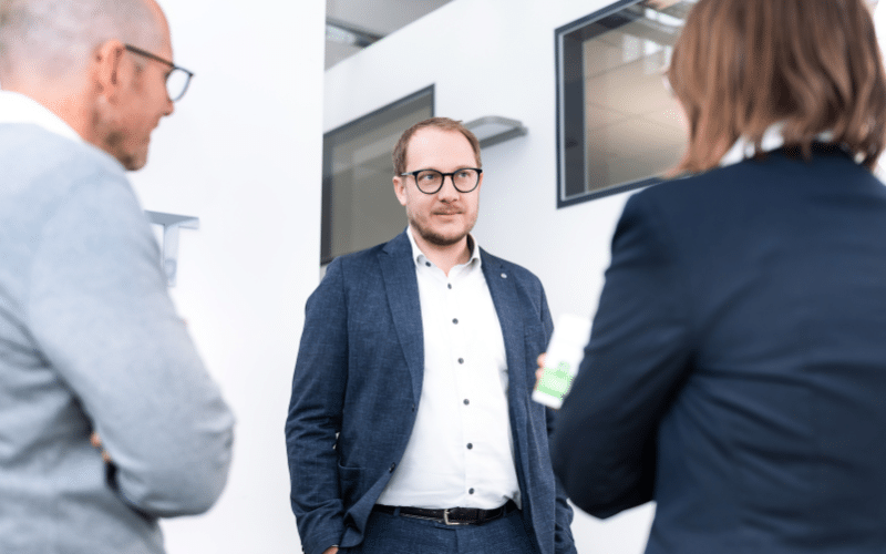 Mann im Anzug unterhält sich mit zwei Kollegen