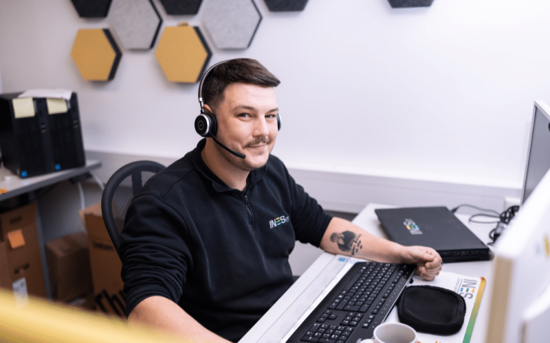 Mann sitzt mit Headset vor dem PC und schaut in die Kamera