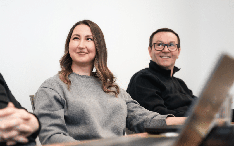 Mann und Frau aus dem Team sitzen im Besprechungsraum und schauen nach vorne