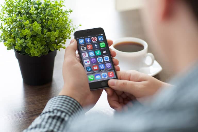 Mann schaut auf Handy, Pflanze und Kaffee auf dem Tisch